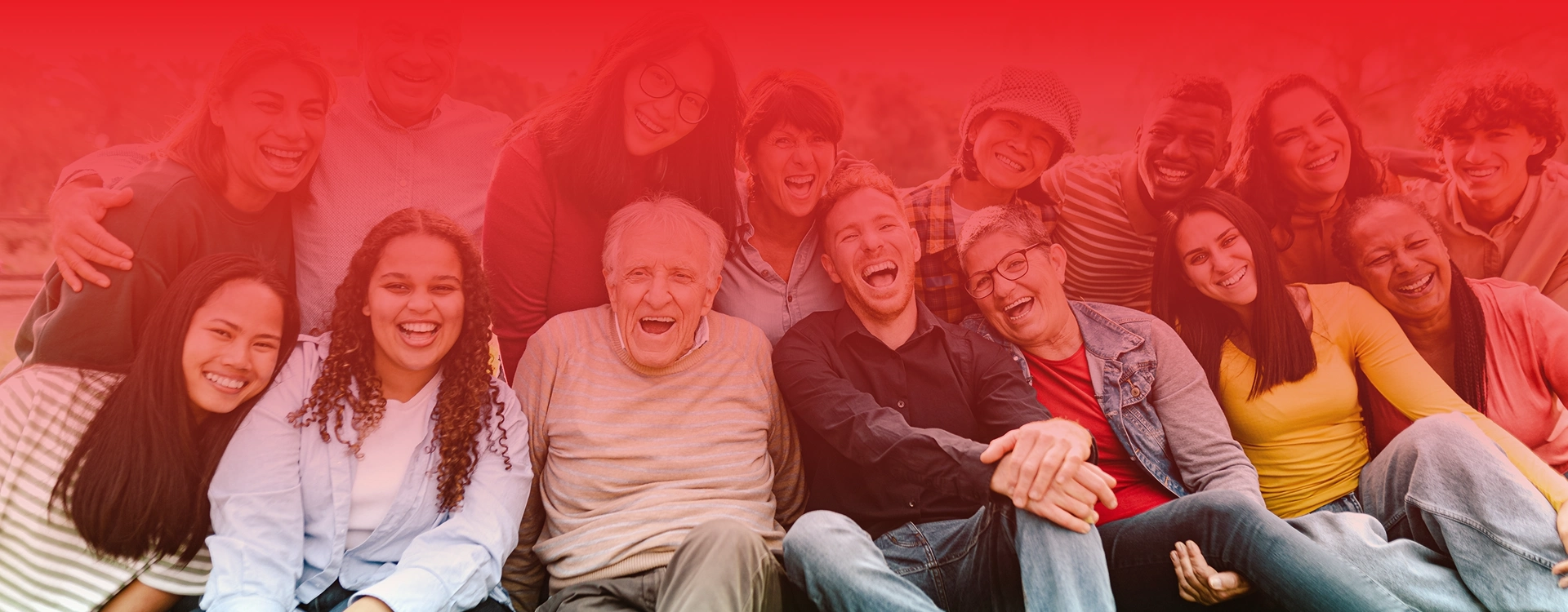 Grupa ludzi różnych pokoleń siedzi razem na dworze i śmieje się do kamery.