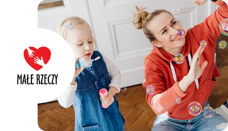 Mała dziewczynka i kobieta bawią się bańkami mydlanymi w domu, obie uśmiechnięte.