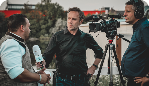 Dziennikarz przeprowadza wywiad z mężczyzną, obok stoi kamerzysta z kamerą.