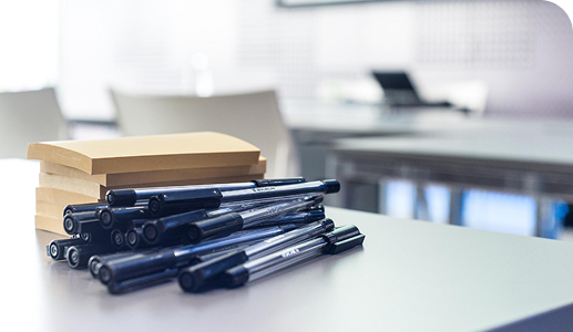 Stos długopisów i notesów na stole w sali konferencyjnej.